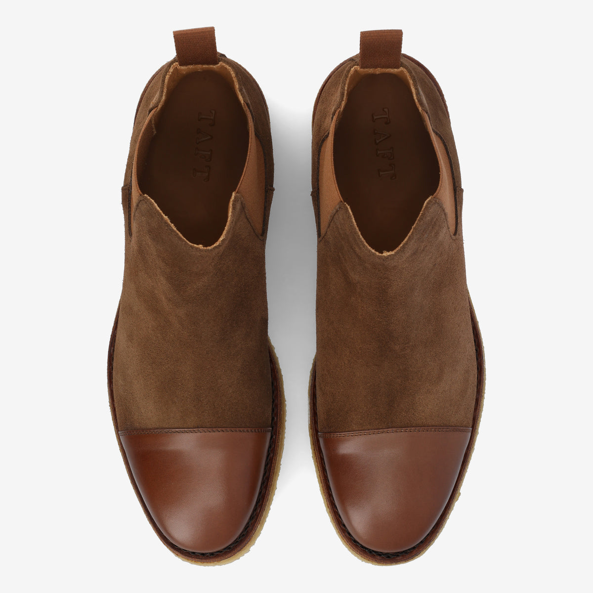 A pair of brown suede and leather cap toe shoes with pull tabs, viewed from above on a white background.