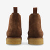 A pair of brown suede ankle boots with pull tabs and beige rubber soles, viewed from the back against a white background.