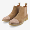 A pair of tan suede Chelsea boots with rubber soles and beige leather toe caps, featuring elastic side panels and pull tabs at the back.