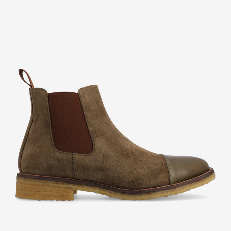 A tan suede Chelsea boot with a brown elastic side panel, pull tab, beige midsole, dark toe cap, and a rubber sole.