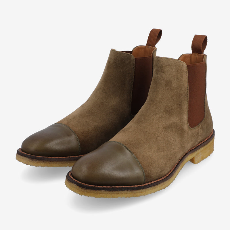 A pair of brown suede Chelsea boots with elastic side panels and brown leather cap toes, featuring a wooden sole and a pull tab on the back.