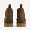 A pair of brown suede boots with pull tabs viewed from the back, showcasing a light tan rubber outsole and minimal stitching details.