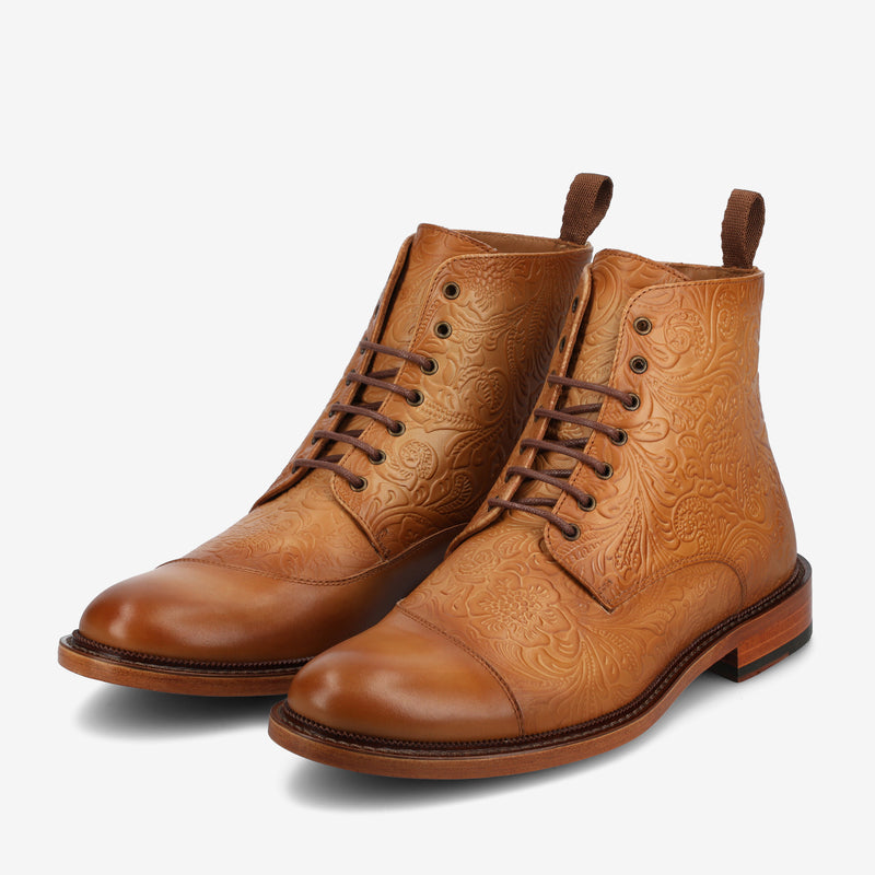 A pair of tan leather lace-up boots with intricate embossed floral patterns on the sides and upper.