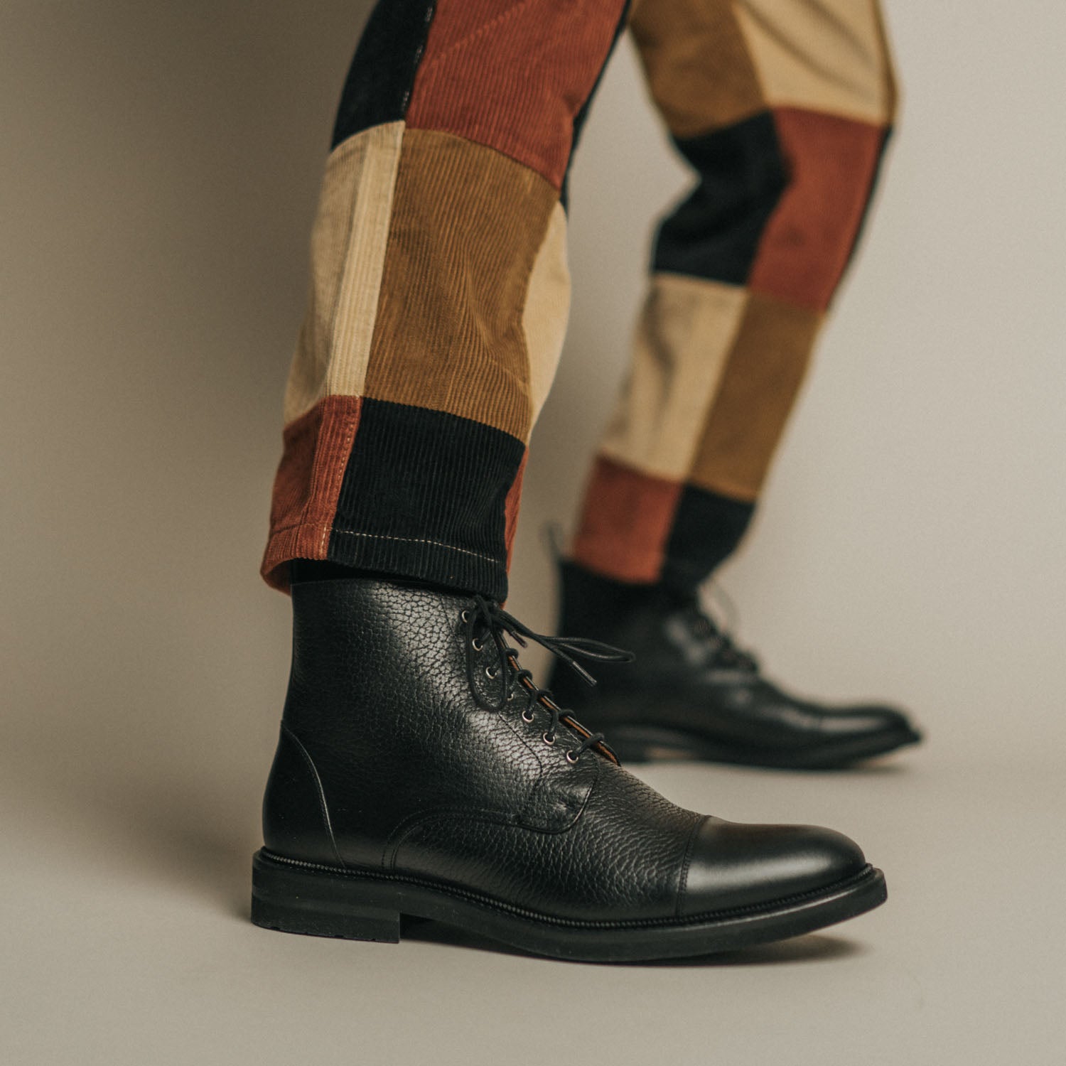 Close-up of a person wearing patchwork pants and black leather boots.