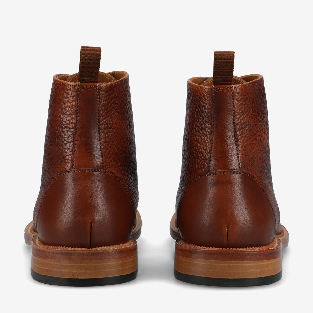 A rear view of a pair of brown leather boots with textured surfaces, featuring pull tabs and wooden soles.