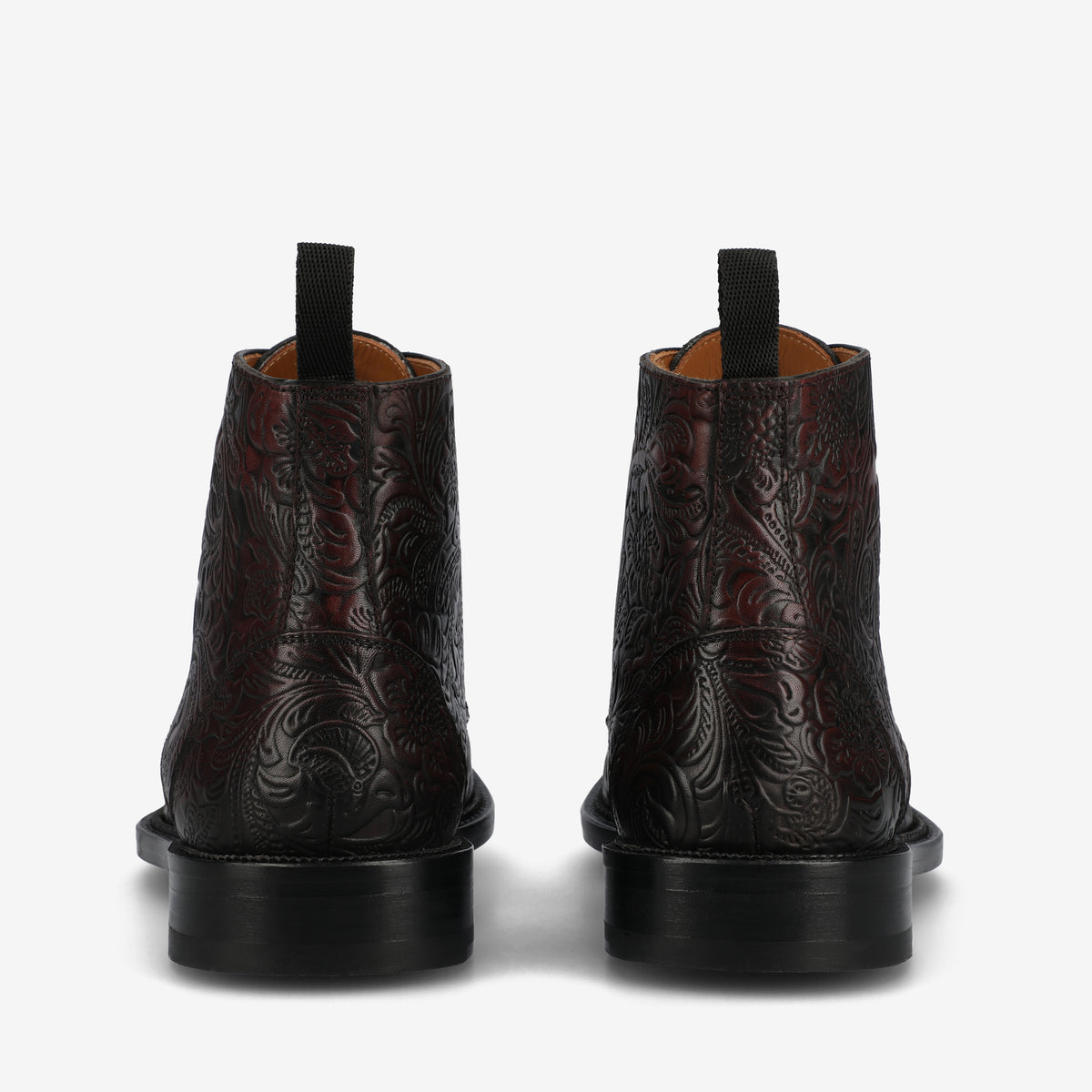 Rear view of a pair of black leather ankle boots with intricate embossed patterns and black pull tabs on a white background.