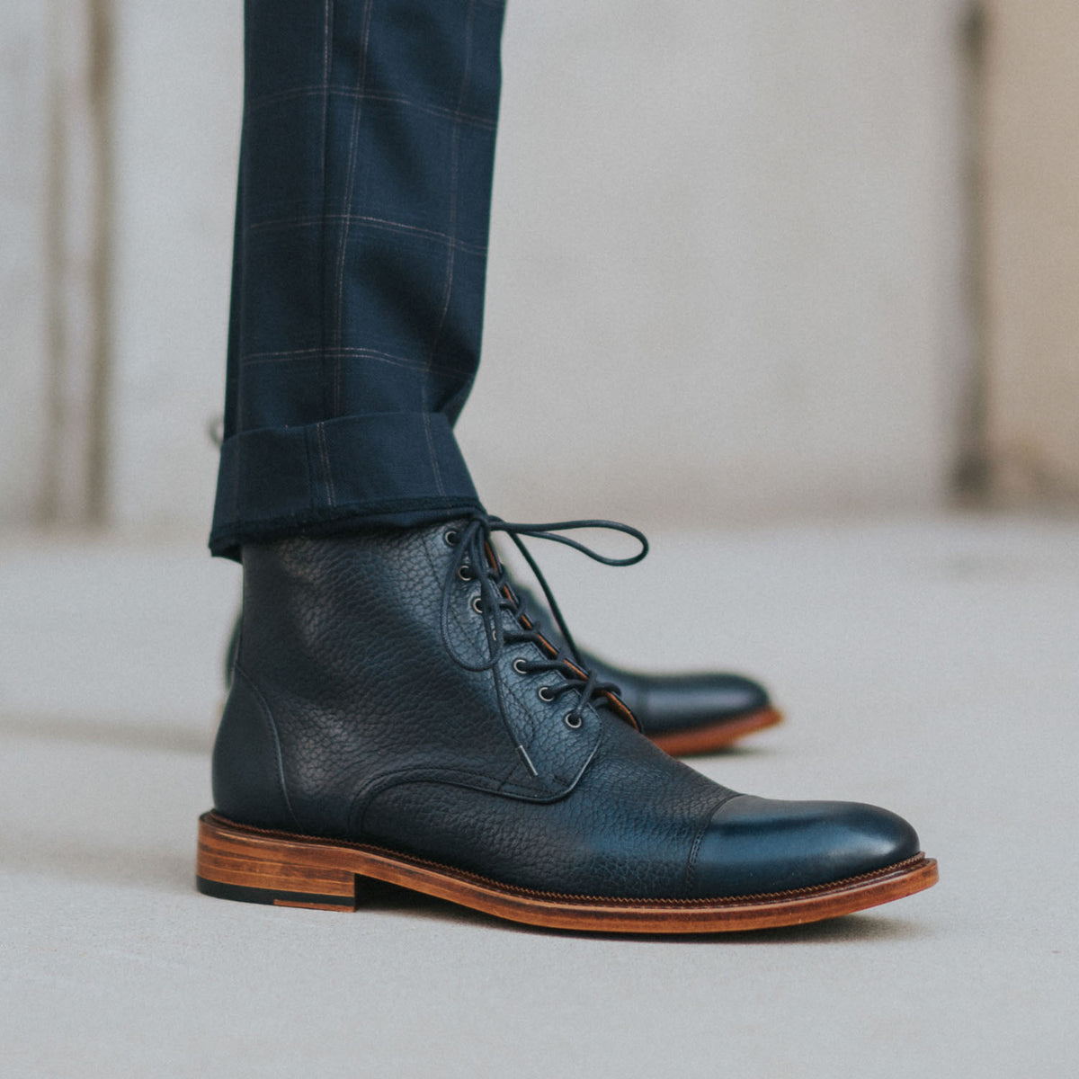 A close-up of a person wearing dark blue plaid pants and black leather lace-up ankle boots with wooden soles.