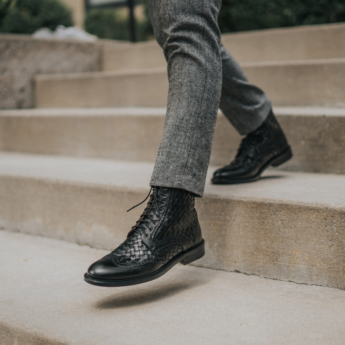 A person wearing gray pants and black leather lace-up boots walks down concrete stairs.