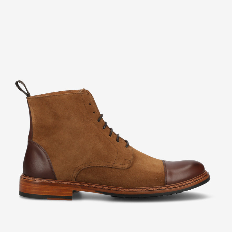 A brown suede boot with a leather cap toe, a wooden midsole, black laces, and a pull tab at the back, displayed on a white background.