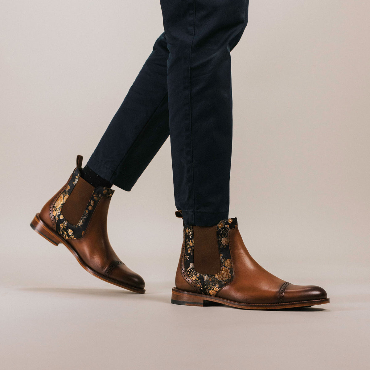 A person wearing dark pants is walking, showcasing brown leather Chelsea boots with floral side panels.