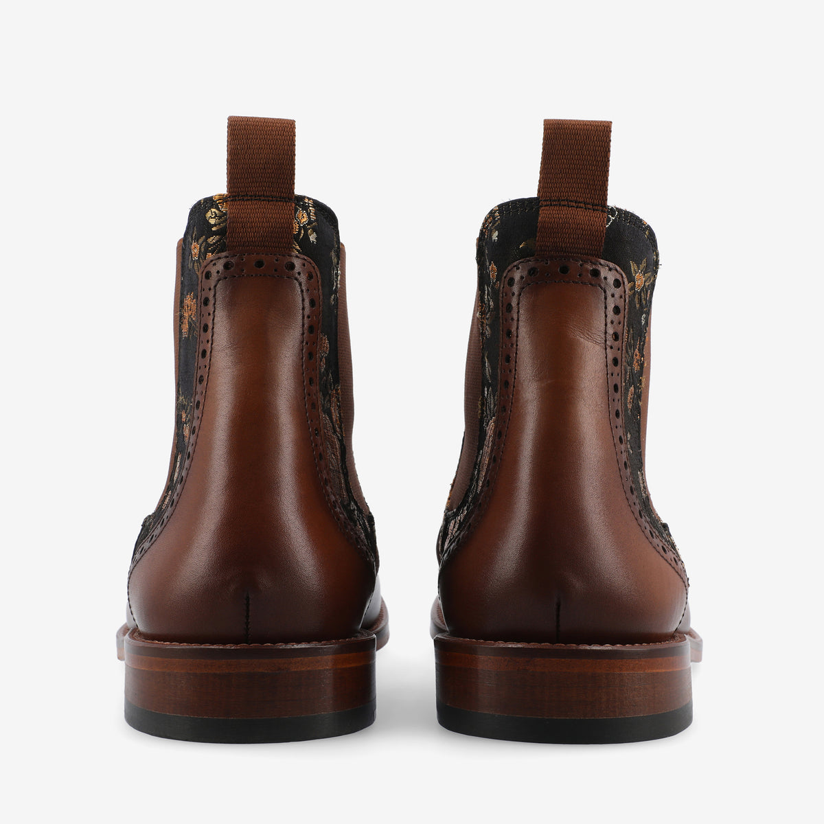 Rear view of a pair of brown leather boots with floral patterned fabric panels and pull tabs.