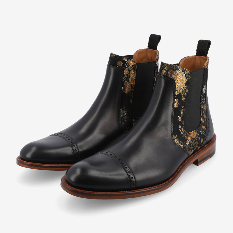 A pair of black leather Chelsea boots with intricate floral embroidery on the sides and brown leather soles.