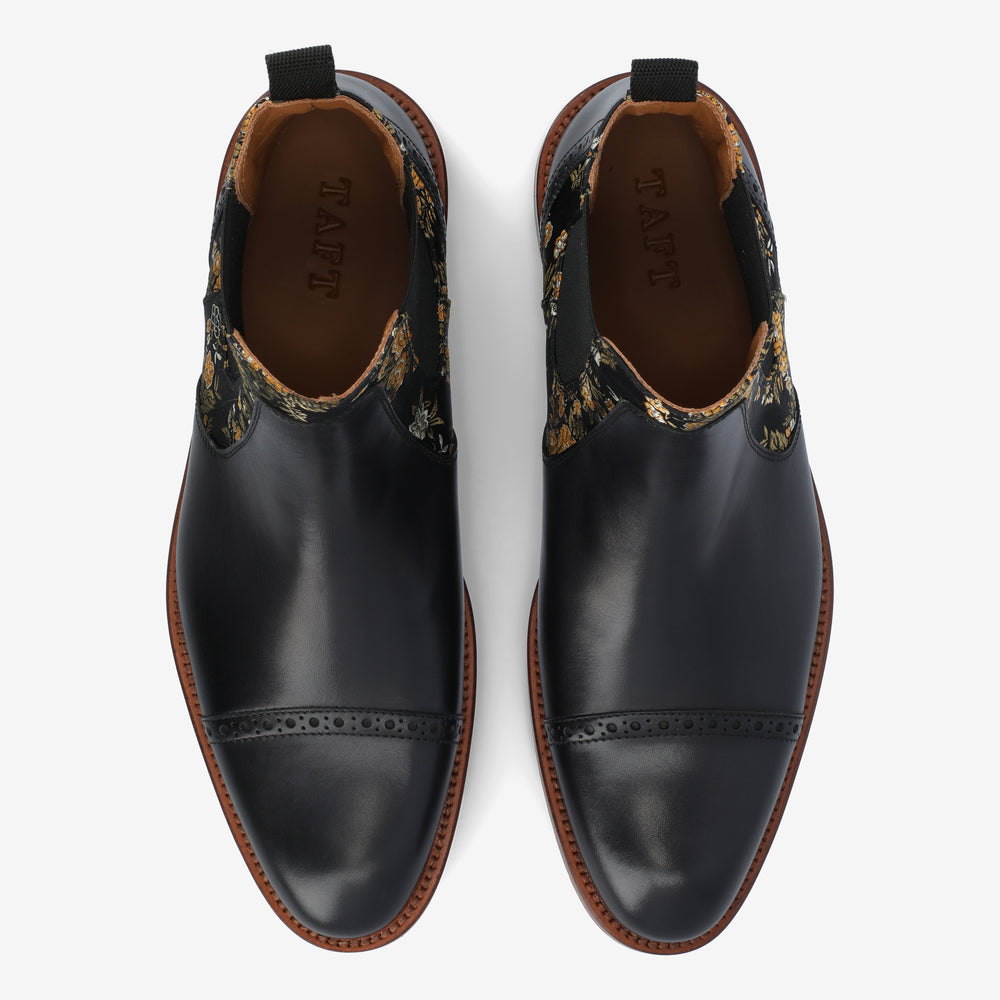 A top-down view of a pair of black leather dress shoes with embroidered floral accents around the collar and brown soles, labeled TAFT on the insole.