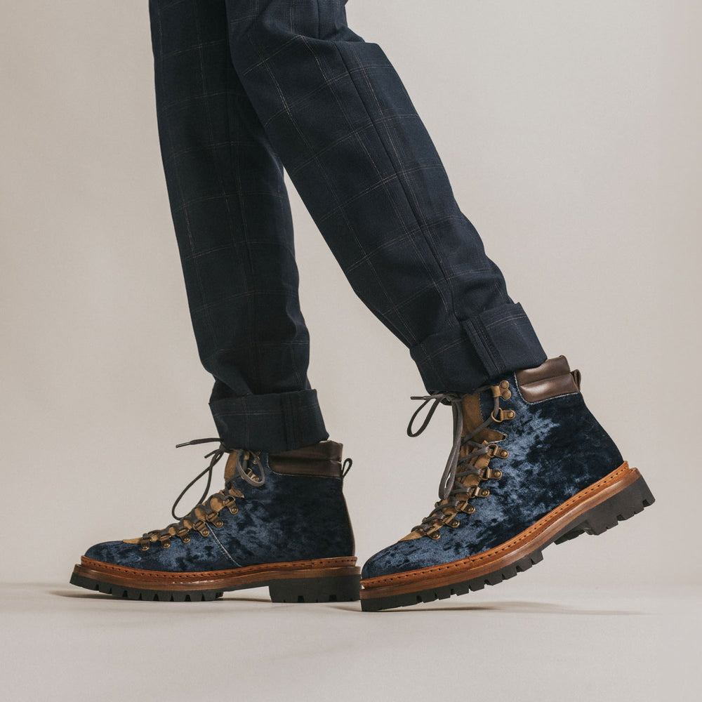 Person wearing dark blue velvet hiking boots with black pants against a neutral background.