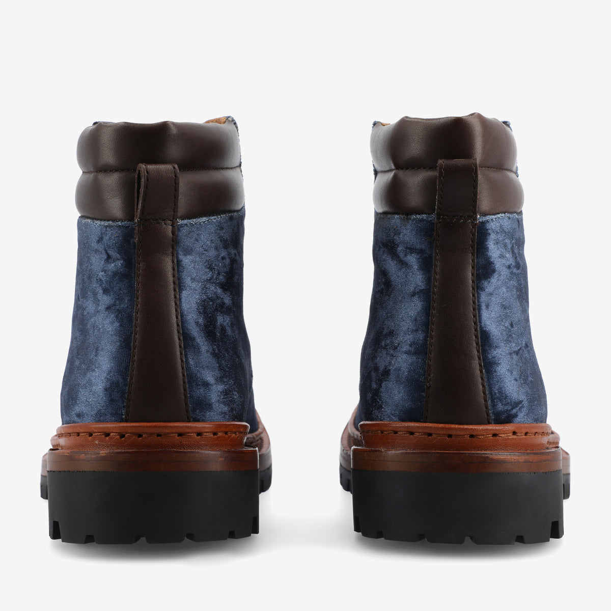 A pair of blue velvet ankle boots with brown leather details and black rubber soles viewed from the back.