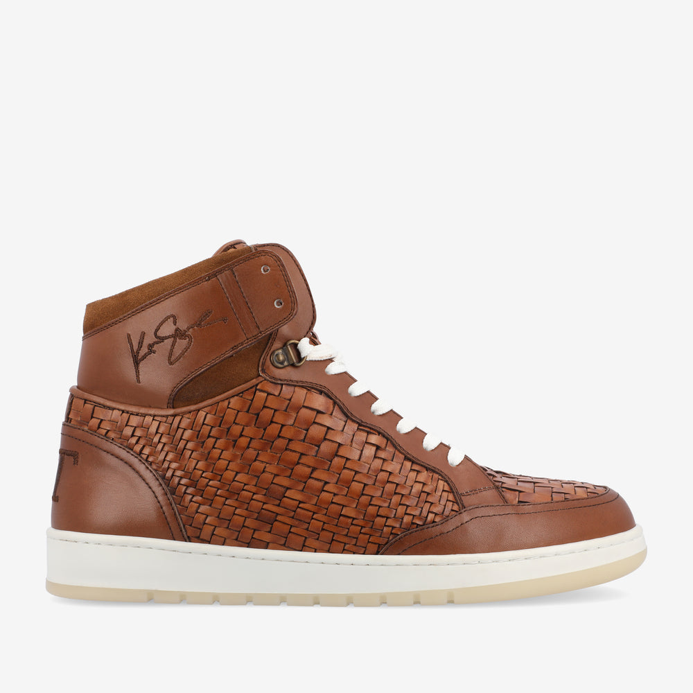 A brown high-top sneaker with a woven leather design, signed with initials on the upper side, white laces, and a white rubber sole.