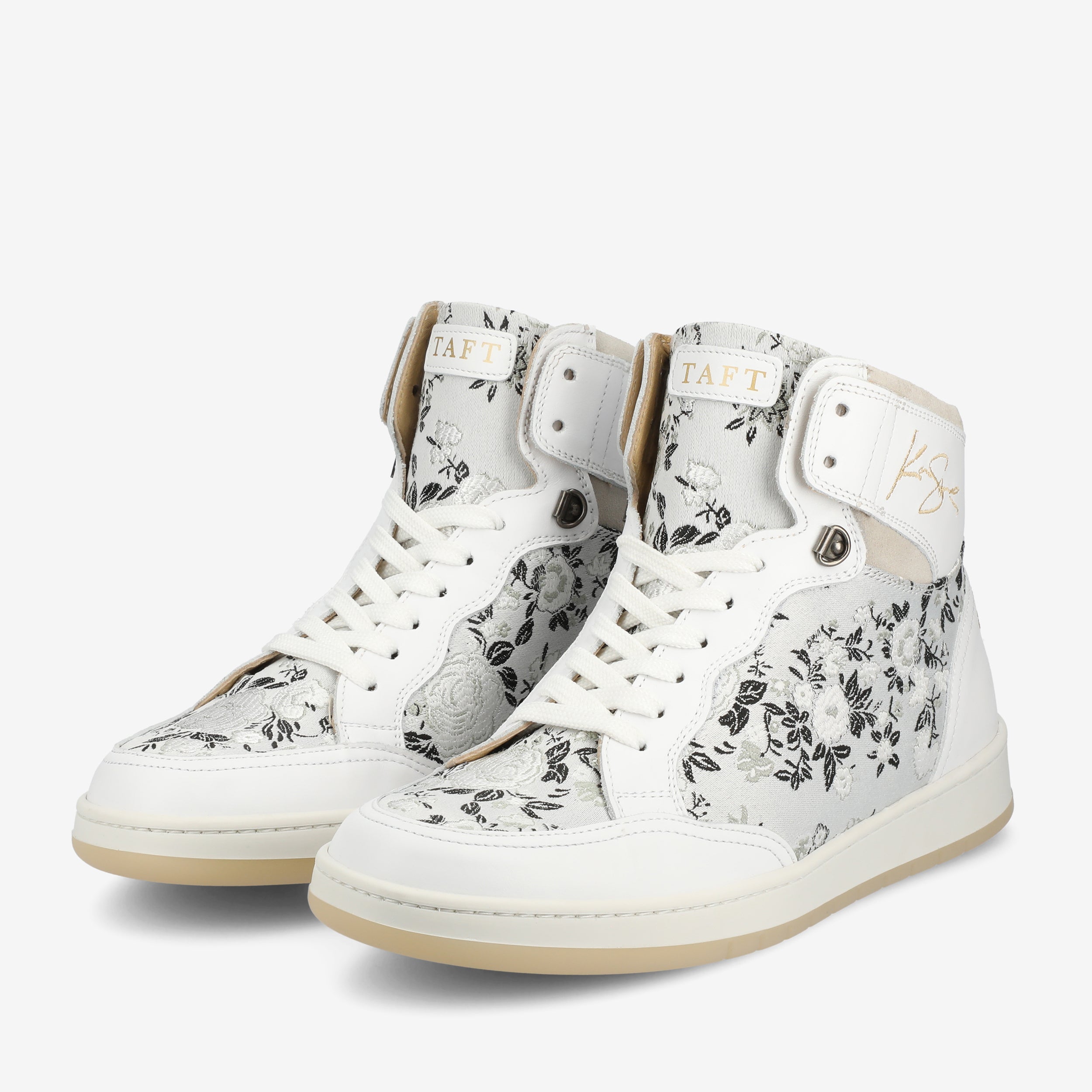 A pair of white high-top sneakers with black floral patterns, white laces, and beige rubber soles. The brand name TAFT is visible on the tongue and side.