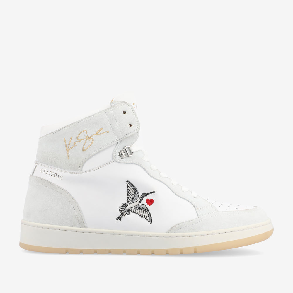 White high-top sneaker featuring a small embroidered bird carrying a heart, gold signature on the ankle, and the number 11172015 on the heel.