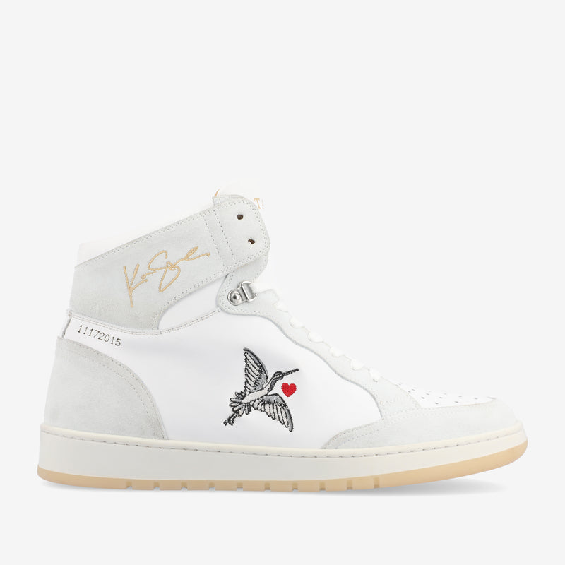 White high-top sneaker featuring a small embroidered bird carrying a heart, gold signature on the ankle, and the number 11172015 on the heel.