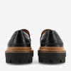 Rear view of black leather loafers featuring a pebbled texture, brown midsole, and thick black rubber outsoles with deep treads.