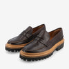 A pair of brown leather loafers with thick black rubber soles and tan stitching on a white background.