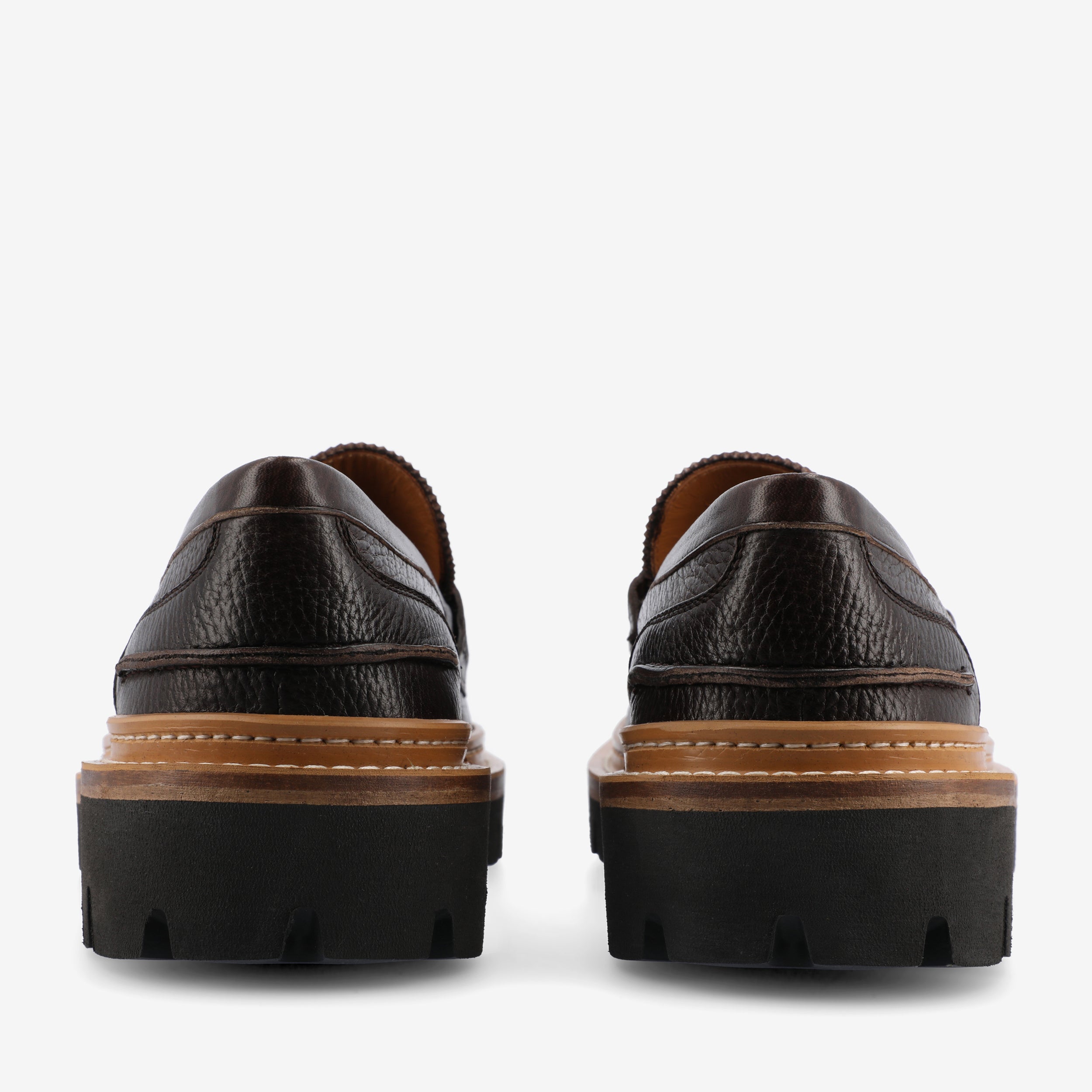 Back view of a pair of brown leather loafers with chunky black rubber soles and visible stitching.