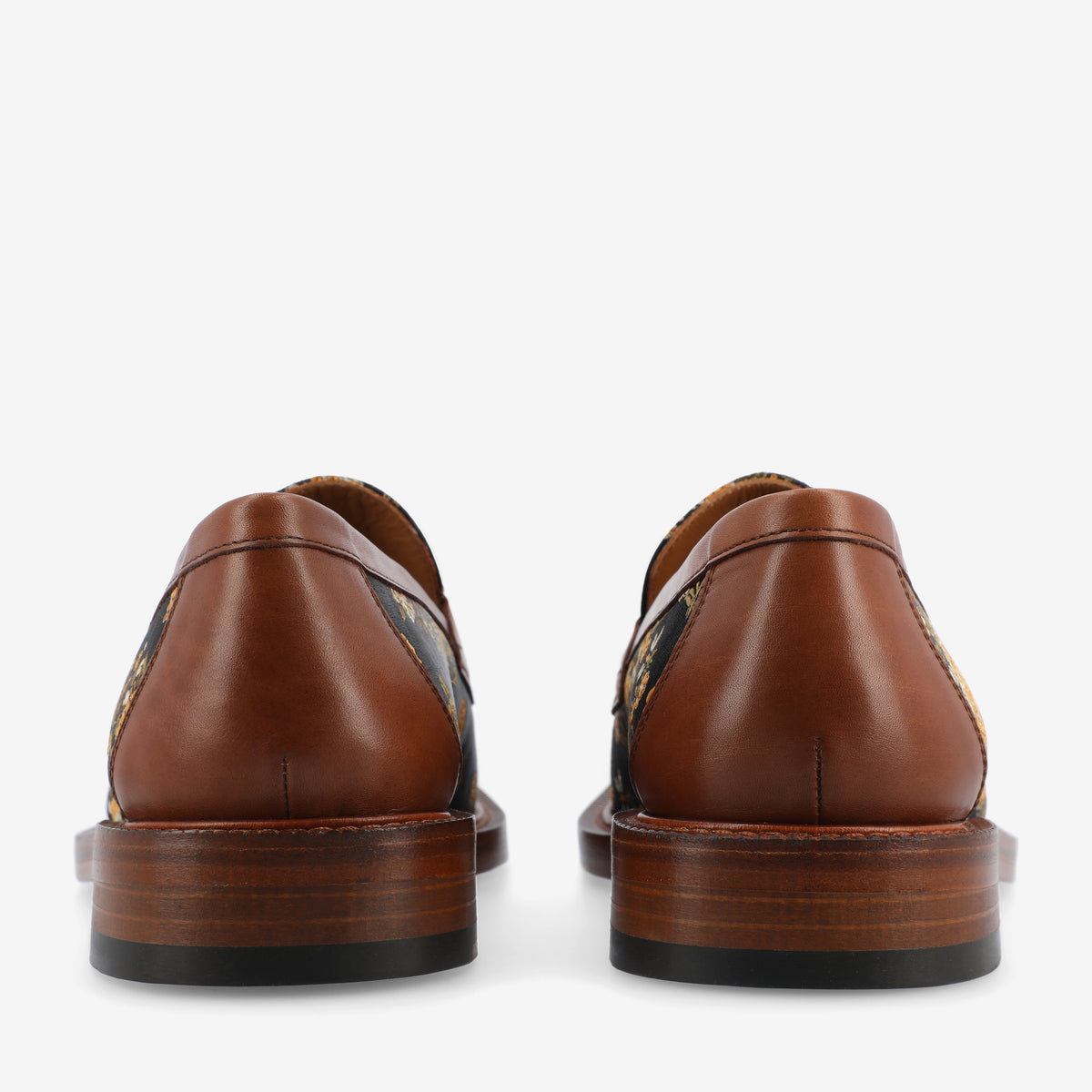 Rear view of a pair of brown leather dress shoes with polished wooden heels, featuring a tapestry-like patterned fabric on the sides.