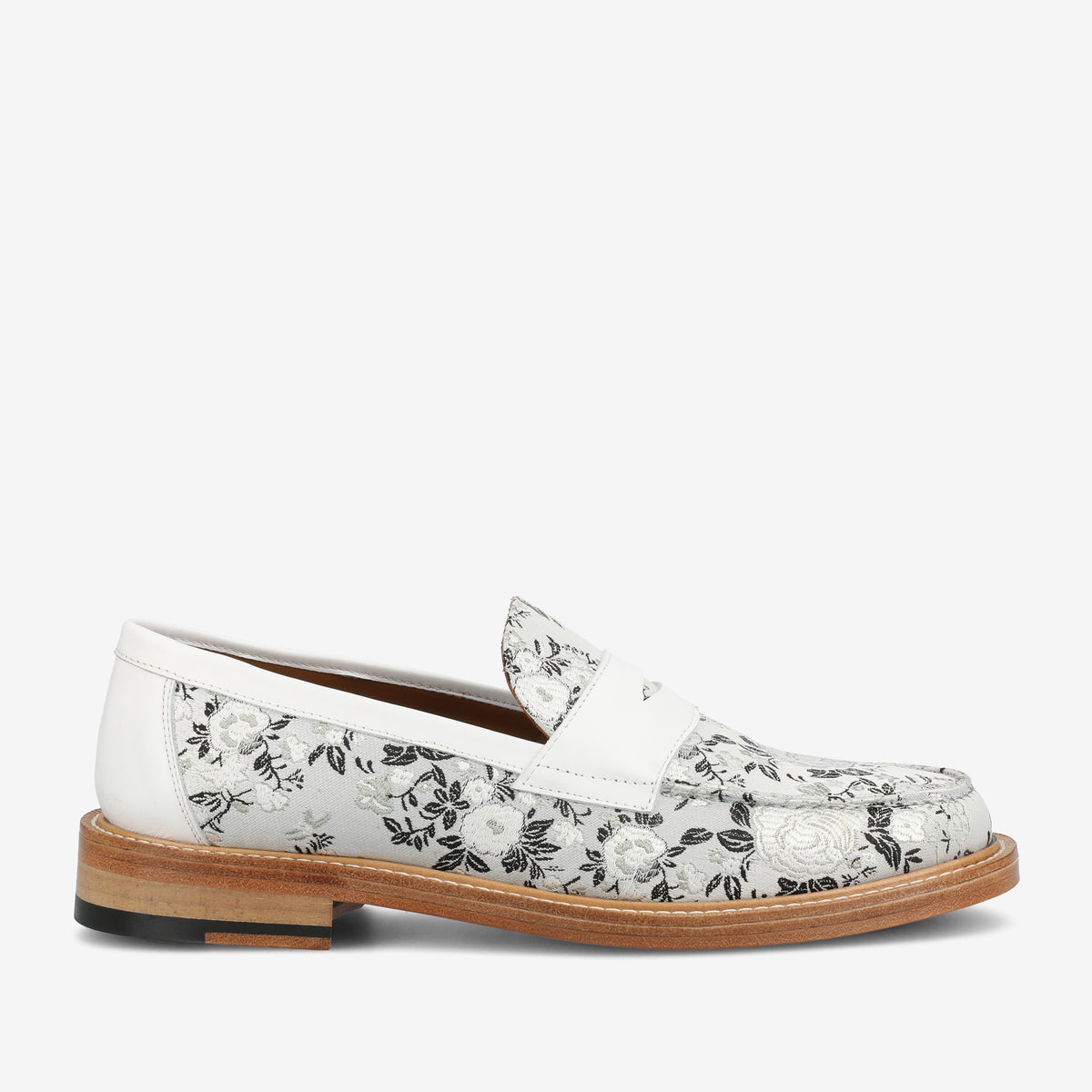 A white leather loafer with a floral design in black and gray, featuring a wooden sole and a low heel.