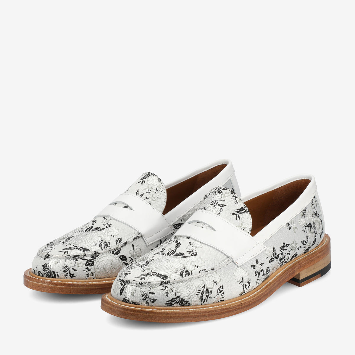 A pair of white loafers with a black floral pattern and light brown wooden soles, displayed on a white background.