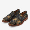 Black loafers with a floral pattern in gold and orange, featuring a leather strap across the top and a brown sole.