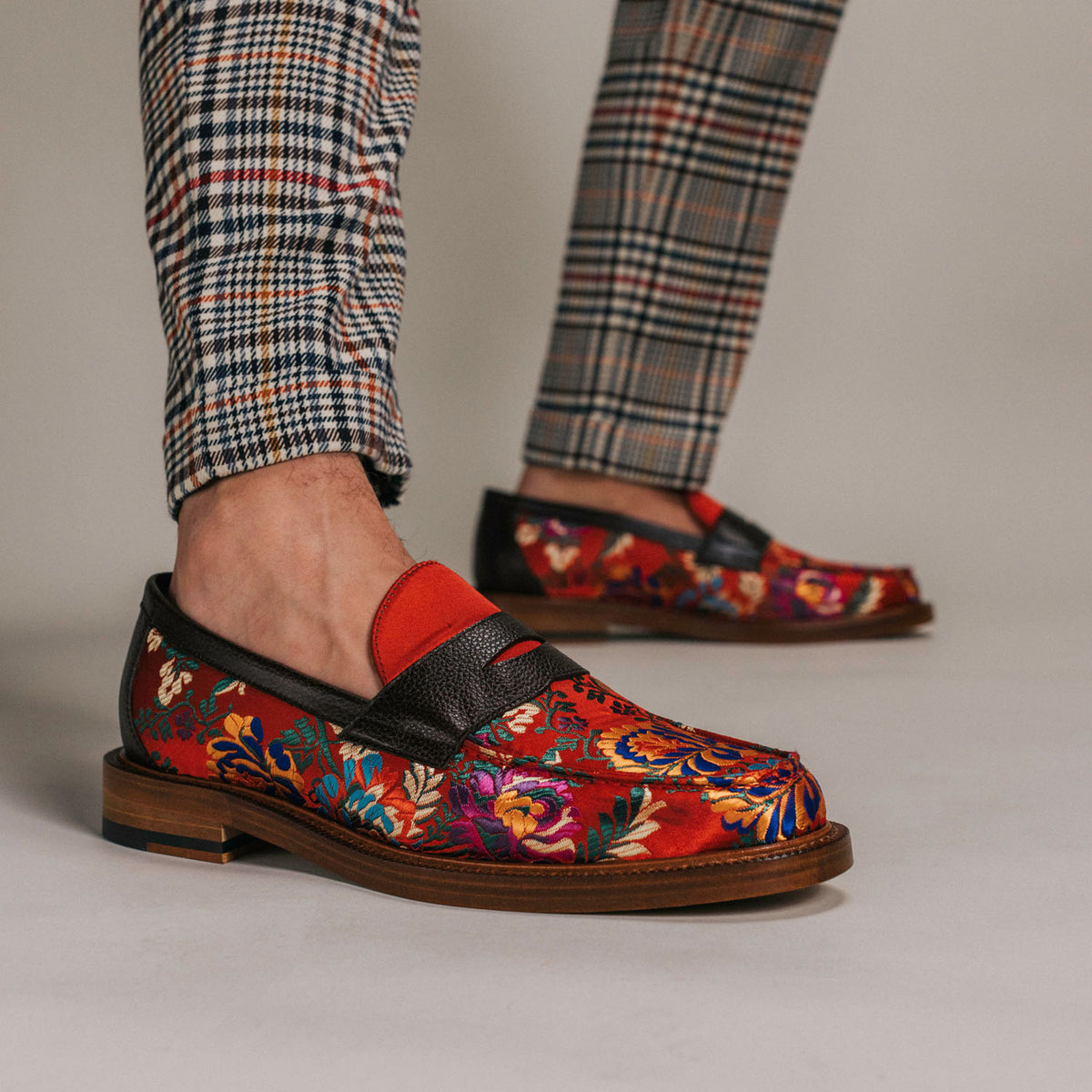 Person wearing plaid pants and colorful floral-patterned loafers with red accents, standing on a light-colored floor.