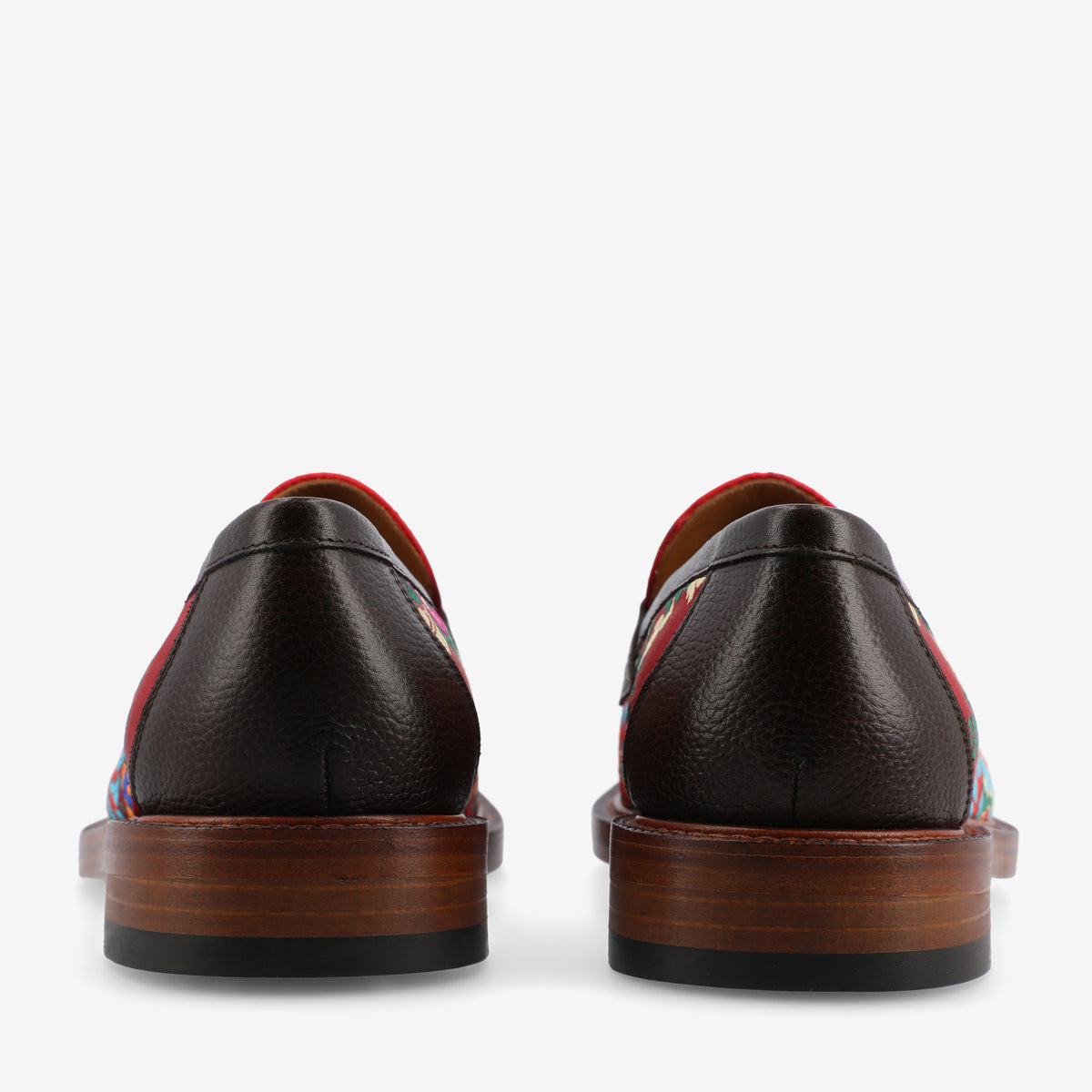 Rear view of a pair of dark brown leather dress shoes with multicolored patterned sides and wooden soles.