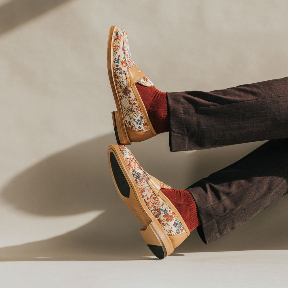 A person wearing brown plaid trousers and red socks with brown leather and floral patterned loafers.