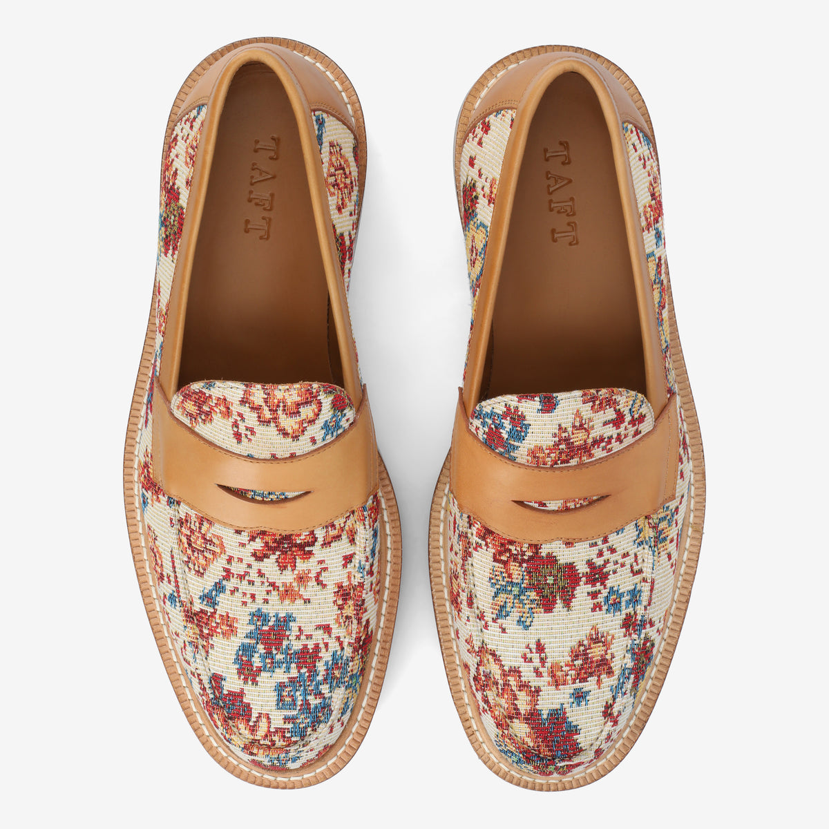 Top view of a pair of loafers with a floral tapestry and tan leather accents. The brand name TAFT is printed inside the shoes.