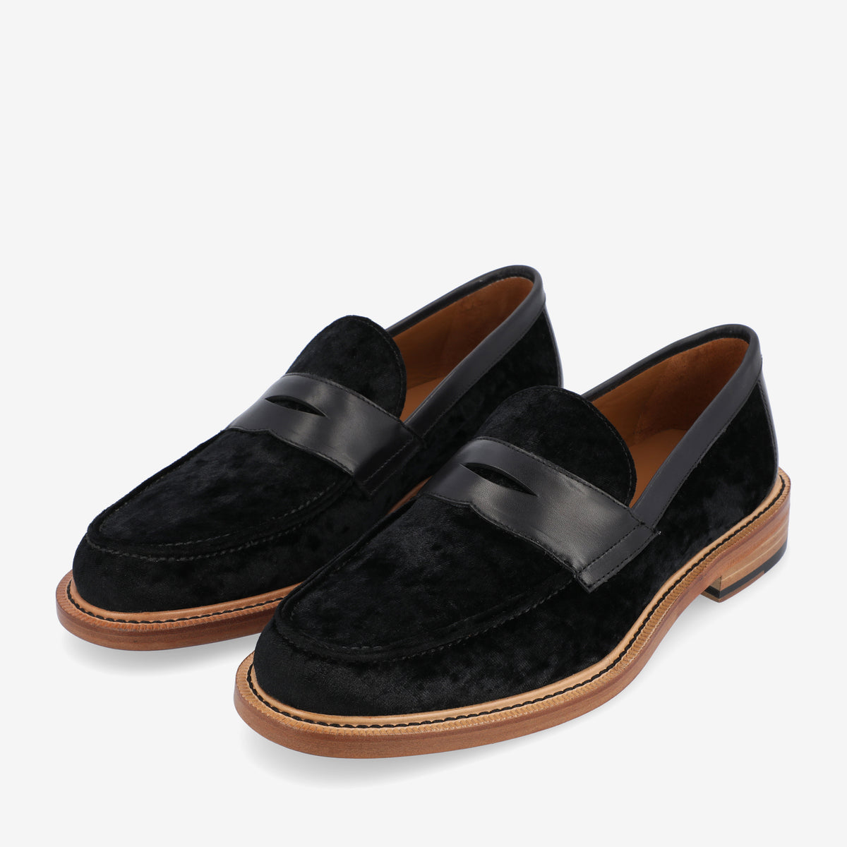 A pair of black velvet loafers with leather straps and brown wooden soles displayed on a white background.