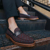 Person wearing black pants and patterned loafers with brown soles, sitting on an outdoor metal staircase.