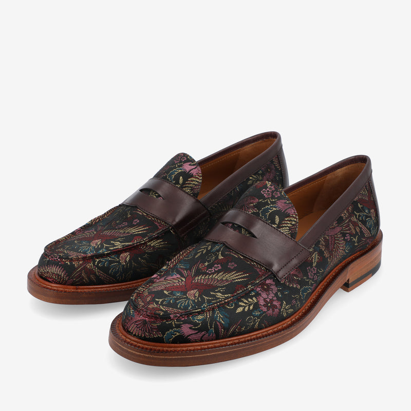 Pair of dark-colored floral patterned loafers with brown leather accents and wooden soles, displayed against a white background.