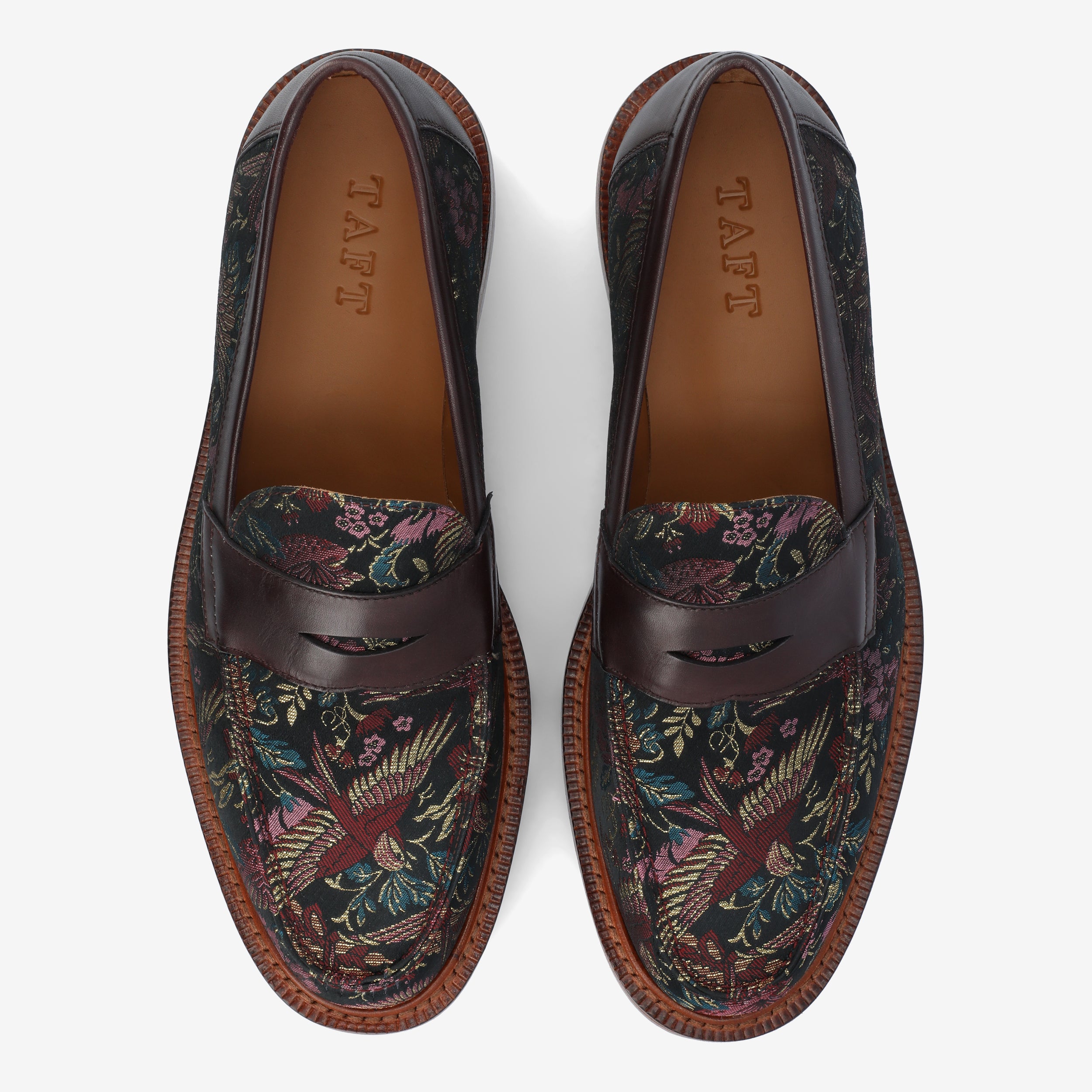 Top view of a pair of loafers featuring dark leather trim and a colorful floral patterned fabric, with the word TAFT branded inside.