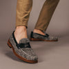 A close-up of someone wearing light brown pants and stylish loafers with a speckled pattern and dark leather accents.