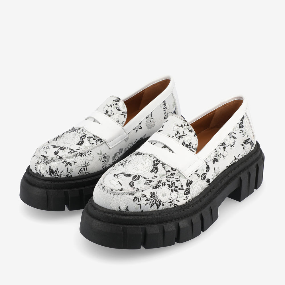 A pair of white loafers with black floral patterns and thick black rubber soles.