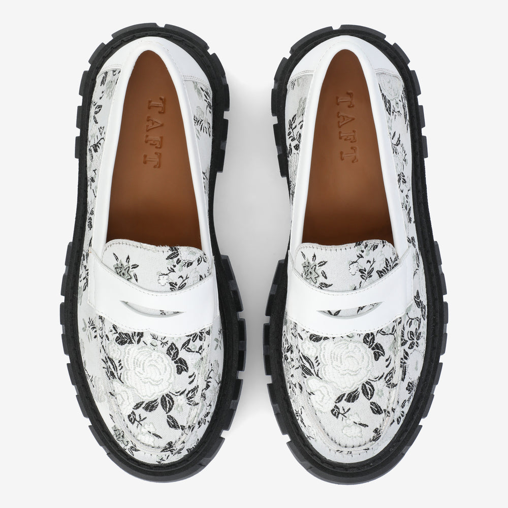 A pair of black and white floral patterned loafers with thick black soles, viewed from above.