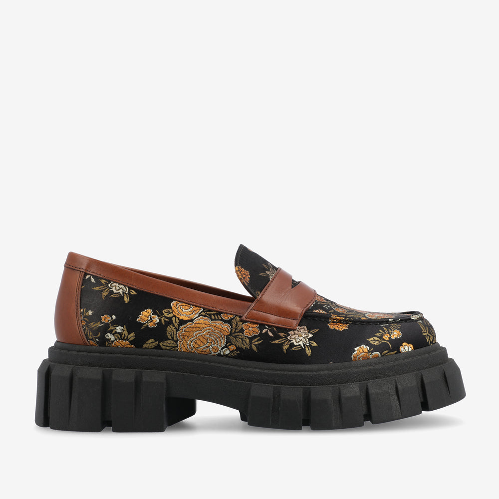 A black loafer with a brown trim and a floral pattern featuring yellow and orange flowers. The shoe has a thick, chunky black sole.