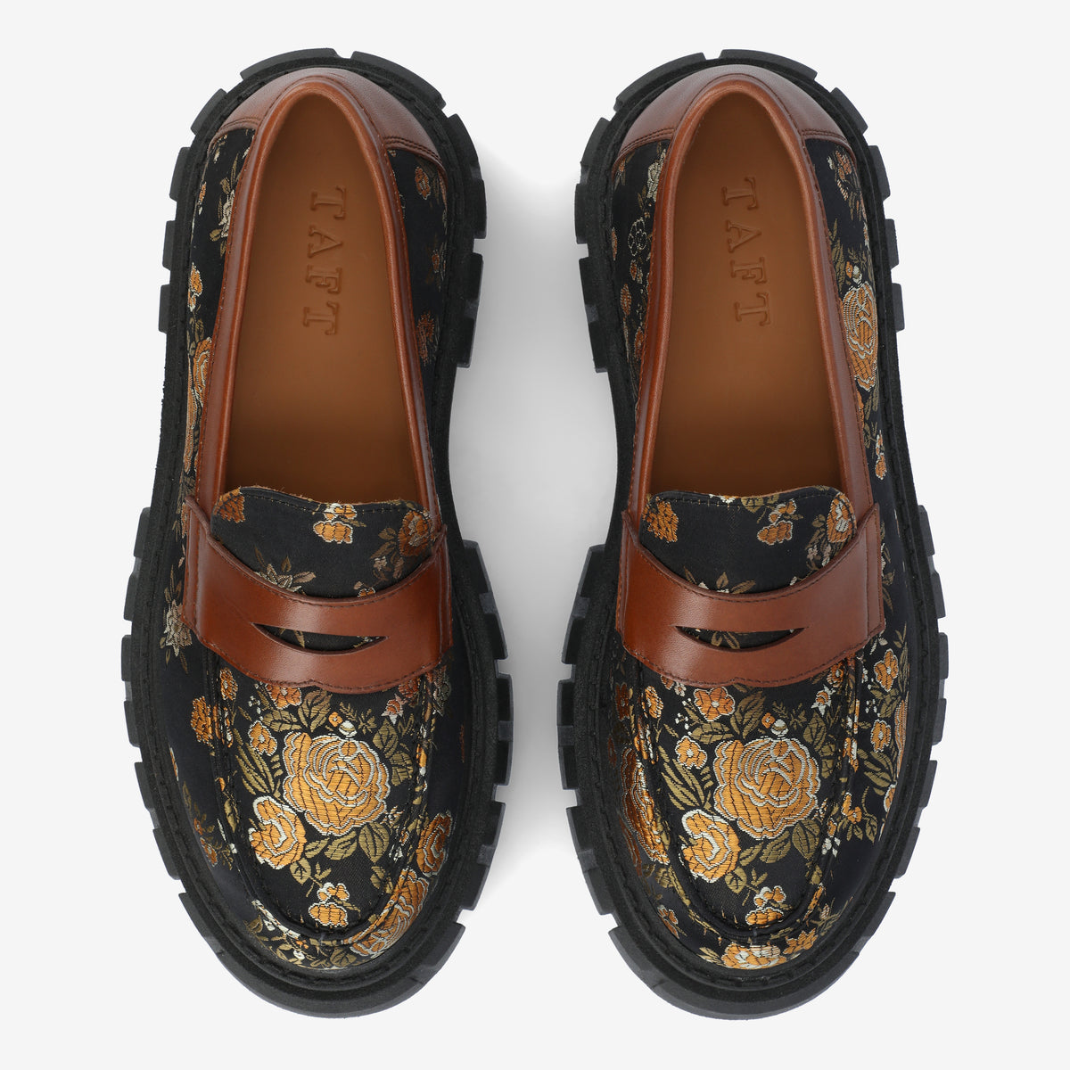 A pair of loafers with black soles, brown leather straps, and a floral pattern with yellow flowers on a black background. The brand name TAFT is embossed on the inner sole.