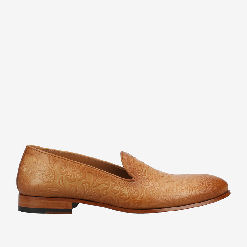 Tan leather loafer with embossed floral patterns, a low heel, and a rounded toe against a white background.