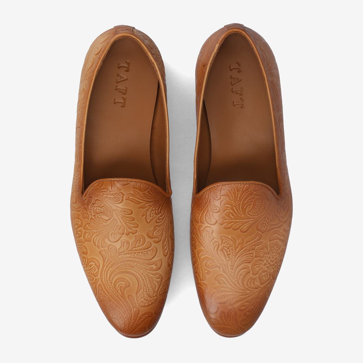 A pair of brown leather loafers with intricate engraved designs on the front and TAFT branded on the inside.