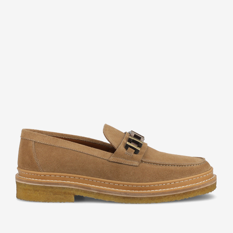 A tan suede loafer with a chunky sole and metal buckle detail on the top.