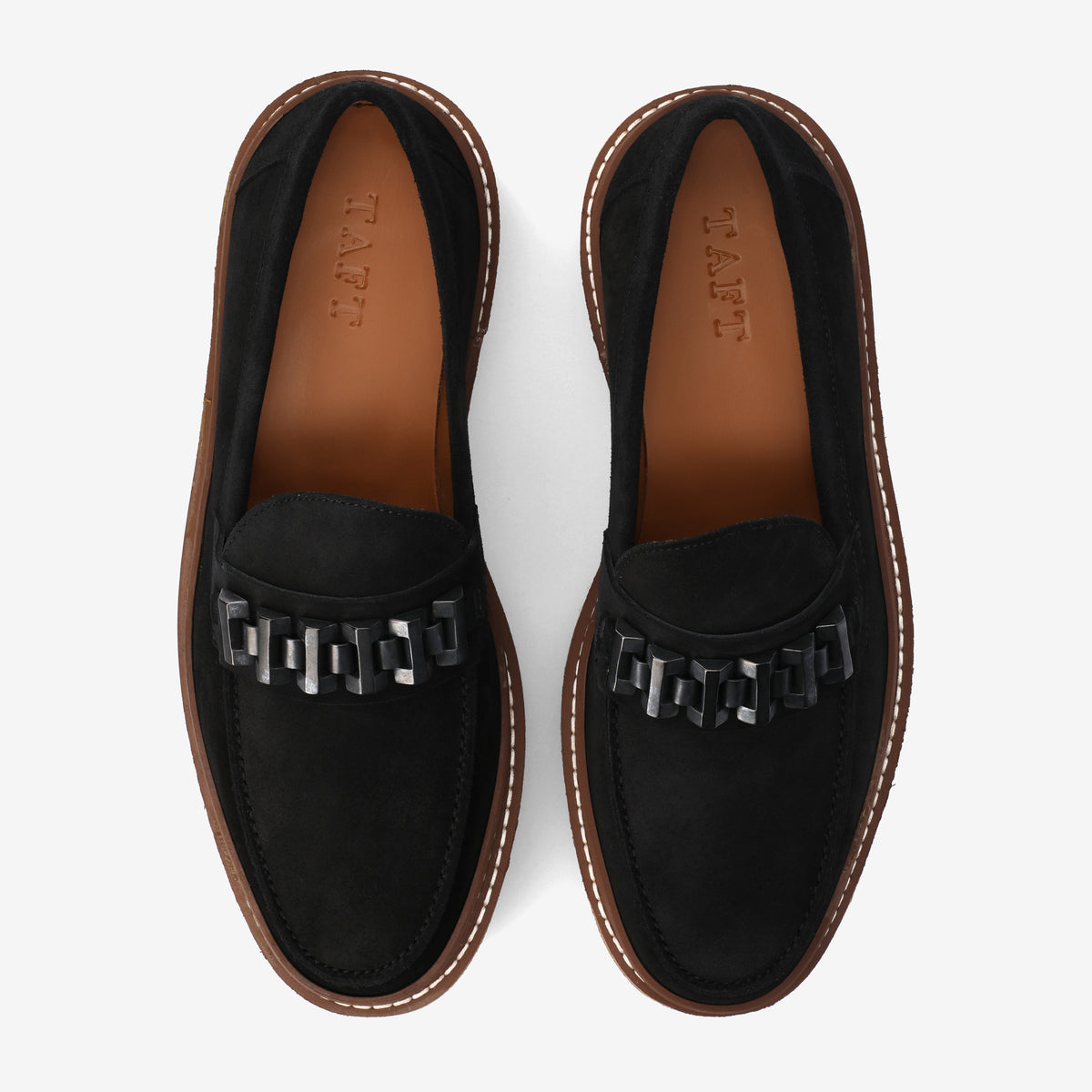 A pair of black loafers with brown soles, featuring a chain detail on the front and TAFT inscribed on the insoles, viewed from above.