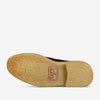 Underside view of a black shoe with a textured beige sole, a rectangular patch featuring text and design stitched onto the sole.