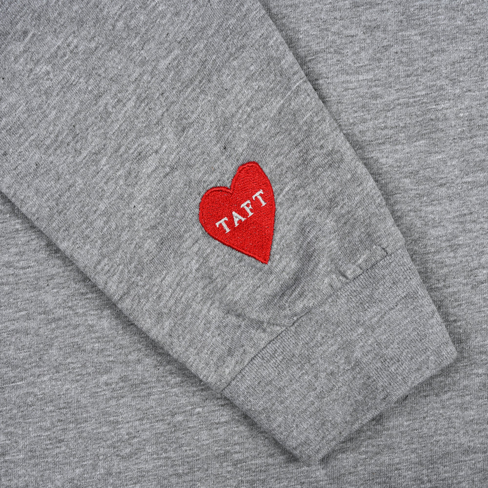 Close-up of the sleeve of a gray garment with a red heart patch that has the word TAFT embroidered in white letters.