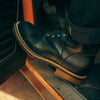 Close-up of a person wearing black leather boots with brown soles, placing one foot inside a vehicle.